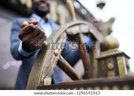 Hand of African-american business leader holding by large wooden sailing wheel while turning it
