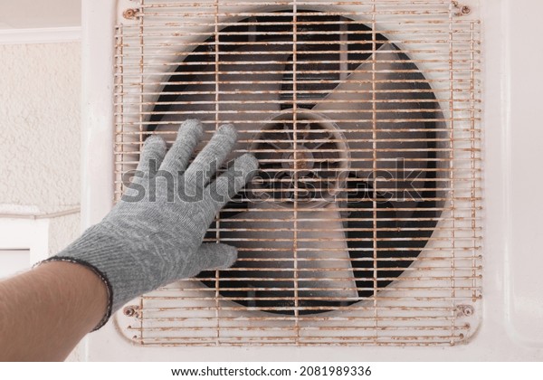 The hand of an air conditioner repair and\
maintenance specialist in a construction glove working with\
air-conditioned old\
equipment.
