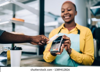 Hand of anonymous black man holding contactless credit card near payment terminal while buying takeaway food in modern cafe - Shutterstock ID 1389412826