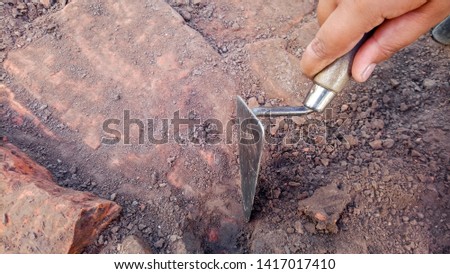 Hand of archaeologist digging by trowel at archaeological excavation, archaeology concept