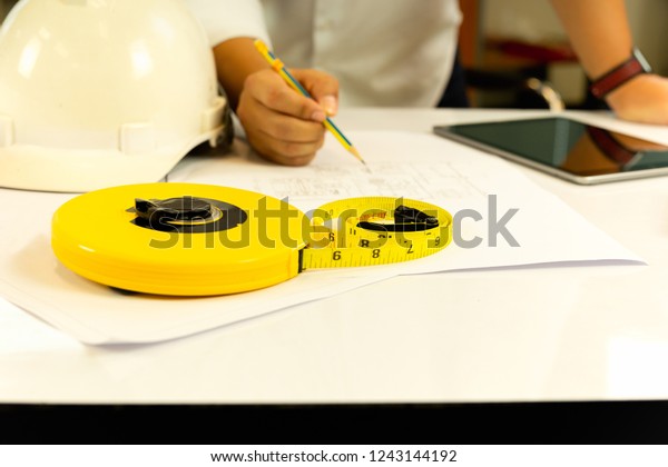 Hand of Architect working on blueprint with tablet\
computer on table