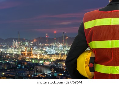 Hand or arm of engineer hold yellow plastic helmet in front of oil refinery industry