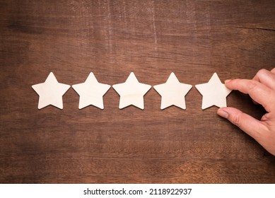 Hand arrange the wooden stars on wood backgroud and put the last one in the row, perfect five stars rating and score