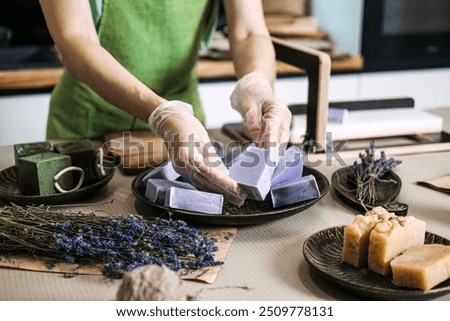 Hand arranging lavender handmade soap bars with dried lavender. Soap making, organic skincare, small business, natural cosmetics, DIY beauty, sustainable living concept