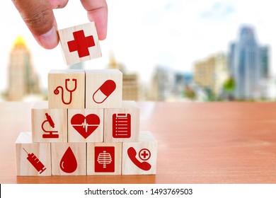 Hand arranging wood block stacking with icon healthcare medical on wooden table against blurred building background , Medical health-care and Insurance for your health concept.