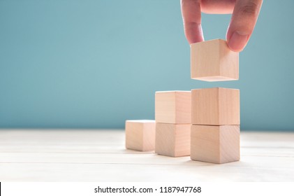 Hand arranging wood cube stacking as step stair. Business concept growth success process on blue background, copy space.