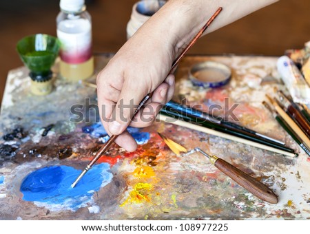 Hand of the artist with a paintbrush and Artistic equipment: paint, brushes, spatula and art palette