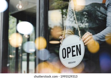 Hand Of Asain Staff Woman Wearing Apron Turning Open Sign Board On Glass Door In Modern Cafe Coffee Shop, Hotel Service, Cafe Restaurant, Retail Store, Small Business Owner, Food And Drink Concept