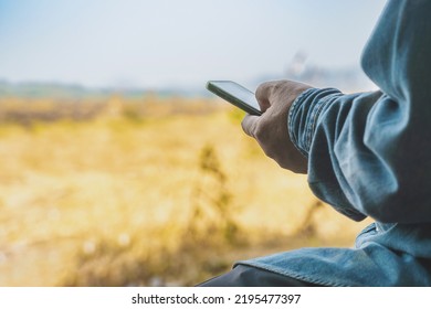 Hand Of Asian Elderly Man Farmer Use Cellphone For Business To Plan Farming In Meadow. Male Farmers Consult With Landowners To Cultivate Crops In Field. Farm And Agricultural Technology And Business.