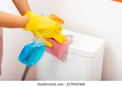 Hand of Asian woman cleaning toilet seat using liquid spray and pink cloth wipe restroom at house, female wearing yellow rubber gloves she sitting cleanup bowl bathroom, Housekeeper healthcare concept
