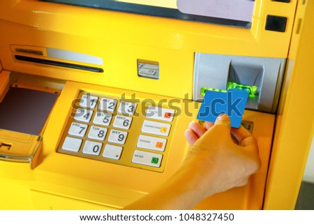 Hand of Asian woman inserting ATM card into yellow ATM machine.