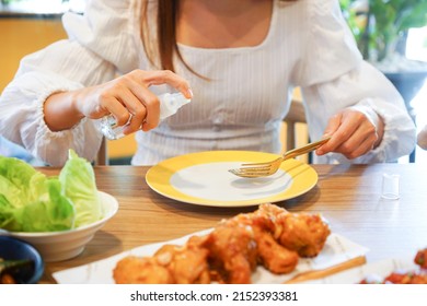 Hand of Asian woman spraying alcohol food grade or pharma grade on dish, spoon and fork in restaurant  before using to cleaning and disinfect of coronavirus and germs. New normal lifestyle concept. 