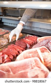 Hand Of Assistant Picking Meat In The Supermarket At A Fresh Meat Counter