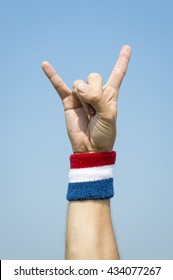 Hand of an athlete making rocker sign against blue sky wearing a USA colors red white and blue sport wristband
