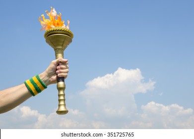 Hand Of An Athlete Wearing Brazil Colors Sweatband Holding Sport Torch Against Tropical Blue Sky