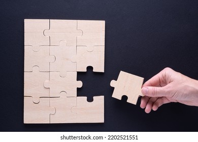 Hand attaches the missing piece of the puzzle. Business concept with wooden jigsaw puzzle on black background. Incomplete wooden puzzles, top view, flat lay. The concept of logical thinking, conundrum