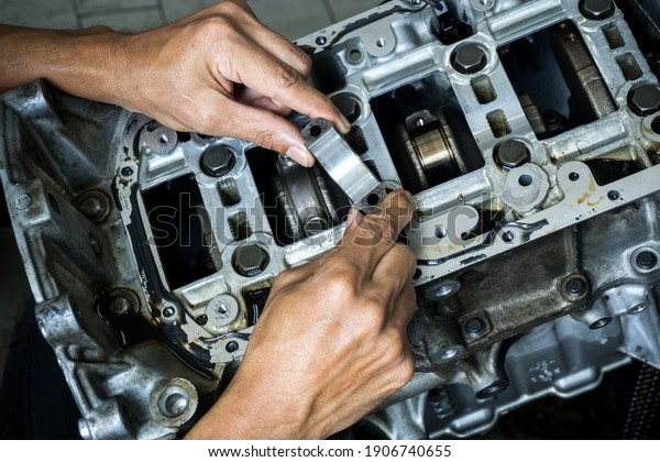 The hand of an auto mechanic picks up the\
engine connecting rod bearing in check with the engine\'s crankshaft\
on background.	