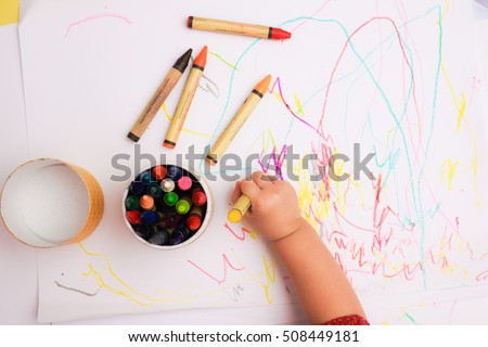 A hand of baby drawing lines and shapes with colorful crayons.