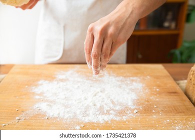 Hand Of Baker Dusting Wheat Flour On Working Surface. Flour Spreading On Wooden Board For Preparing Dough. Studio Shot. Side View. Homemade Bakery And Nutrition Concept