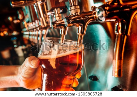 Hand of bartender pouring a large lager beer in tap. Bright and modern neon light, males hands. Pouring beer for client. Side view of young bartender pouring beer while standing at the bar counter.