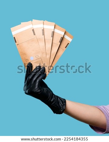 Hand of Beautician holds kraft aseptic paper bags flat self-sealing. Empty space. Cosmetologist in black latex glove on blue background in studio