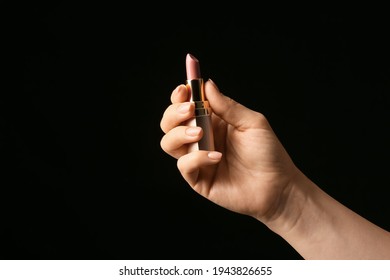 Hand with beautiful manicure holding lipstick on dark background