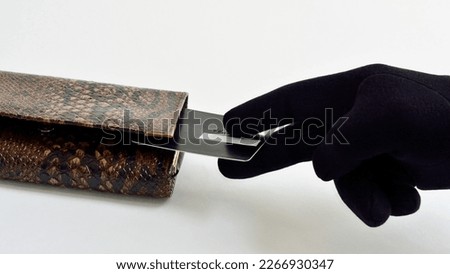 A hand in a black glove steals a bank card from a wallet. The concept of stealing money from bank cards.