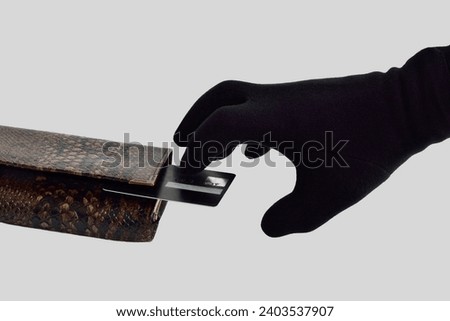 A hand in a black glove steals a bank card from a wallet. The concept of stealing money from bank cards.