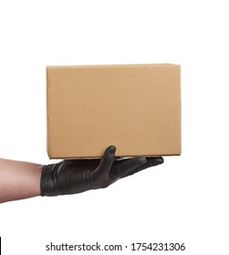 Hand In Black Latex Glove Holds A Cardboard Box Of Brown Kraft Paper On A White Background, Safe And Contactless Delivery Of On-line Orders During Epidemics