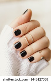 hand with black manicure and rings on the phalanges on short nails in a white sweater on a light background. The concept of a stylish and warm winter.