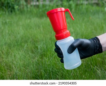 Hand In Black Nitrile Glove Holding A Teat Dip Cup For Udder Cow Disinfection On The Green Grass Background, Copy Space. Milking Practice