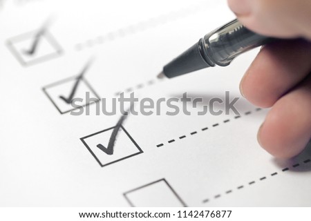Hand with black pen marking on checklist box.