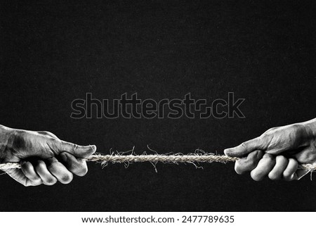 Hand in Black and White Pulling Rope to Opposite Sides, Paper Textured Black Background with Copy Space