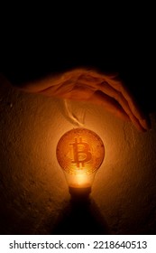 Hand Blocking The Light From The Light Bulb With Bitcoin Coins. Business Money Protection Concept.