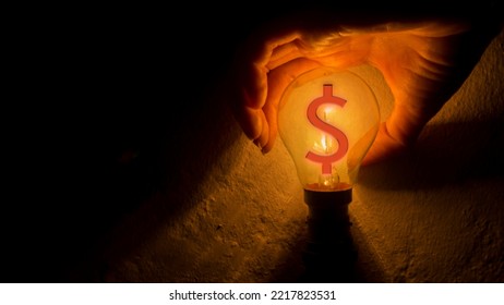 A Hand Blocking Light From A Light Bulb With A Dollar Sign. Business Money Protection Concept.