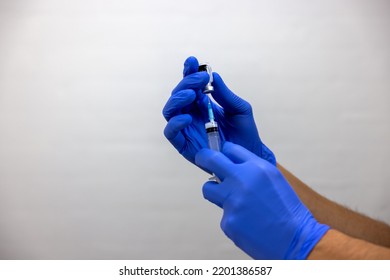 A Hand In Blue Glove Preparing A Vaccination, Medicine, Mixture, Antidote Against Disease, Virus, Bacteria, Toxin. A Syringe Is Filling Up.
