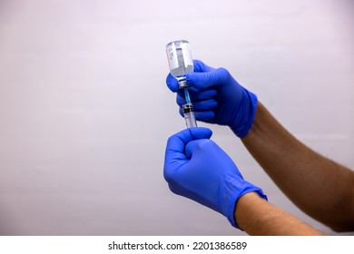 A Hand In Blue Glove Preparing A Vaccination, Medicine, Mixture, Antidote Against Disease, Virus, Bacteria, Toxin. A Syringe Is Filling Up.