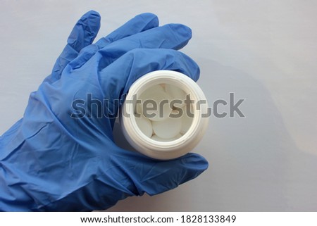 Hand in blue glove with tablets on white background. Doctor holding bottle with white pills. Selective focus 
