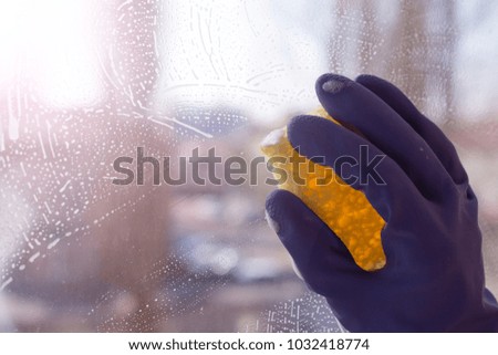 Hand blue glove wash window with yellow sponge. World Cleanup Day concept, copy space, close up, selective focus