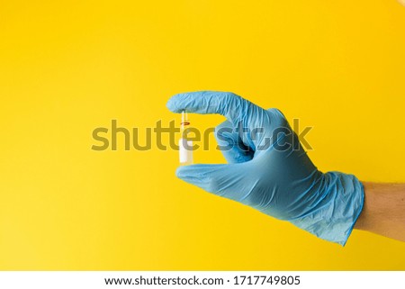 

hand in a blue latex glove holds a glass ampoule on a bright yellow background