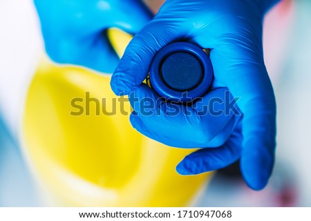 Hand with blue latex gloves opening a yellow bottle of bleach.