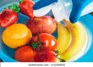 Hand with blue latex gloves pouring bleach into a plastic bowl with different fruits and water in the kitchen. Disinfecting fruits and vegetables to prevent the spread of the coronavirus - Shutterstock ID 1712330410