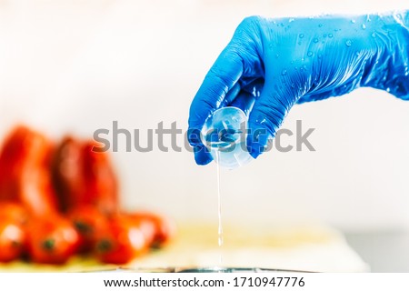 Hand with blue latex gloves pouring disinfectant liquid to decontaminate fruit and vegetables from viruses. Washing the fruit with bleach.