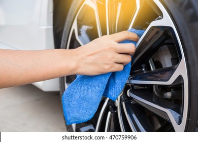 Hand with blue microfiber cloth cleaning car wheel.