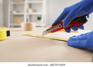 Hand in blue protective glove using a utility knife and ruler to cut material on a wooden table, close up