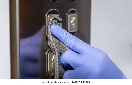 Hand in blue rubber glove holding gray microfiber cleaning cloth make cleaning and disinfection for good hygiene of elevator buttons. Prevention of coronavirus or covid-19 infection