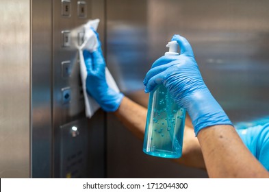 Hand In Blue Surgical Gloves Using Disinfectant From The Bottle Spraying An Elevator Push Button Control Panel.Disinfection,cleanliness And Healthcare,Anti Bacterial And Corona Virus (COVID-19). 