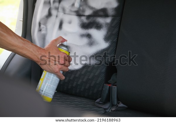 hand with a bottle of cleaning agent sprays foam on\
the seats of the passenger compartment of a car, takes care of\
salon of the auto
