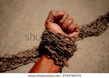 A hand bound by old chains in the blazing sunlight.