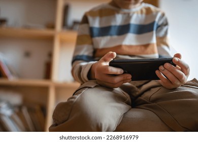 hand of boy caucasian child hold smartphone mobile phone at home play video games childhood and growing up technology addiction concept use smartphone app for online browsing or watch video - Shutterstock ID 2268916979